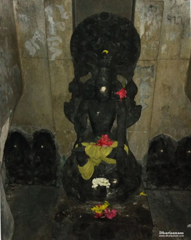 A seated dark stone idol with a hooded backdrop and flowers, flanked by small carved niches on either side.