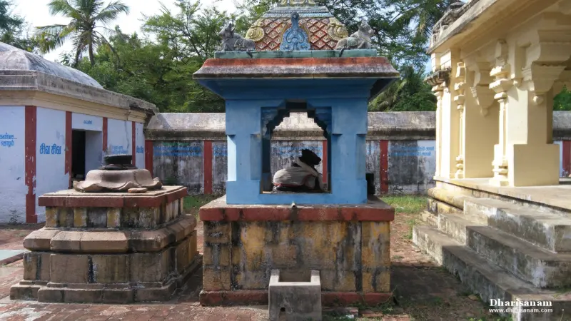 Small blue shrine holding a Nandi in front of a yellow pillared hall, with a stone pedestal beside it