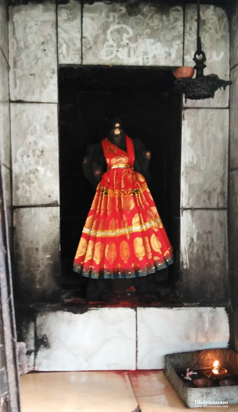 A dark stone figure dressed in a red and gold gown inside a niche, with a lit lamp on the floor