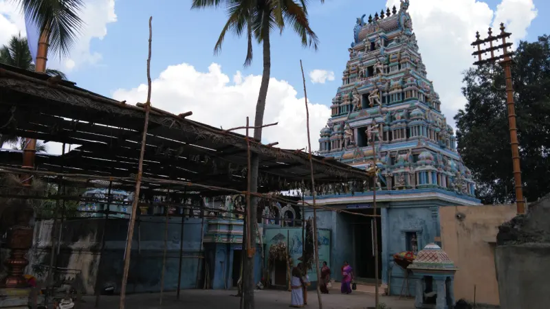 Temple tower beside a thatched shed, with devotees walking in the courtyard
