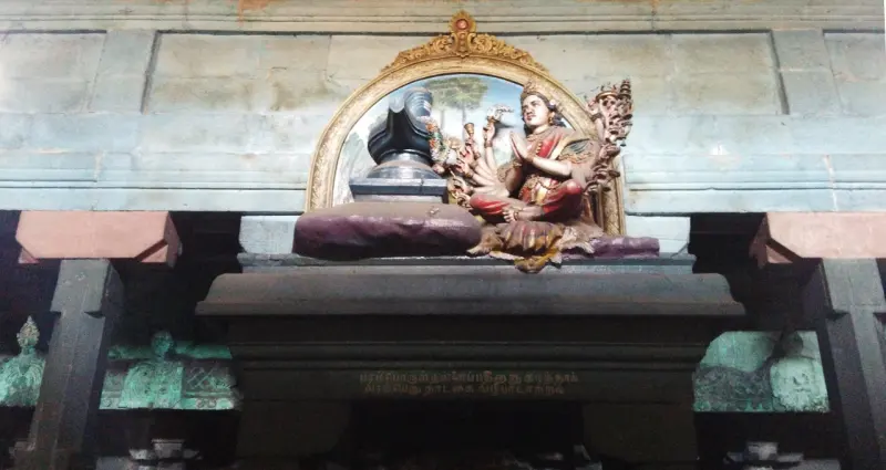 Painted woman with folded hands before a bent lingam