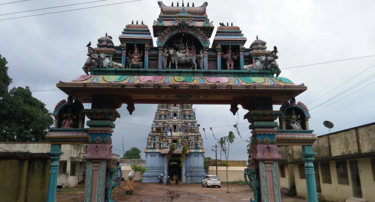 A painted entrance arch with sculpted figures on top; a tower stands behind it and a car is parked below.