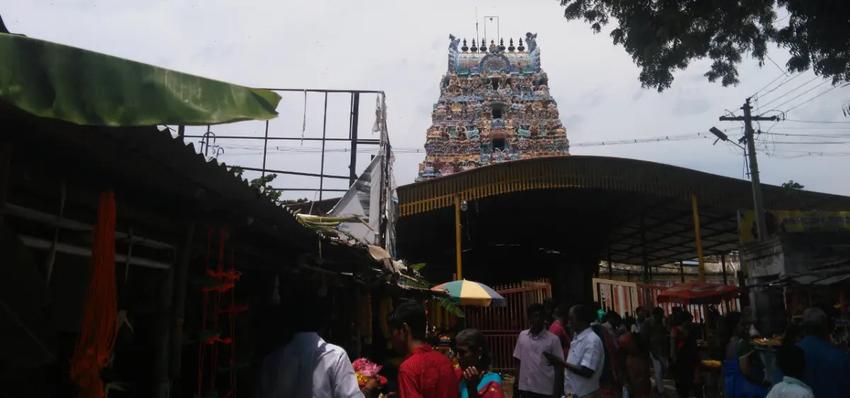 A tiered tower covered in painted figures behind roadside stalls, with devotees in the foreground