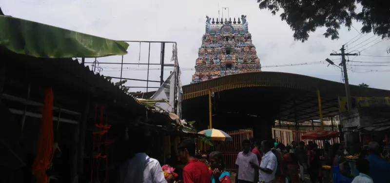 A tiered tower covered in painted figures behind roadside stalls, with devotees in the foreground