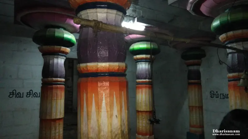 Pillars painted in orange, purple and green in a whitewashed hall with Tamil words on the wall