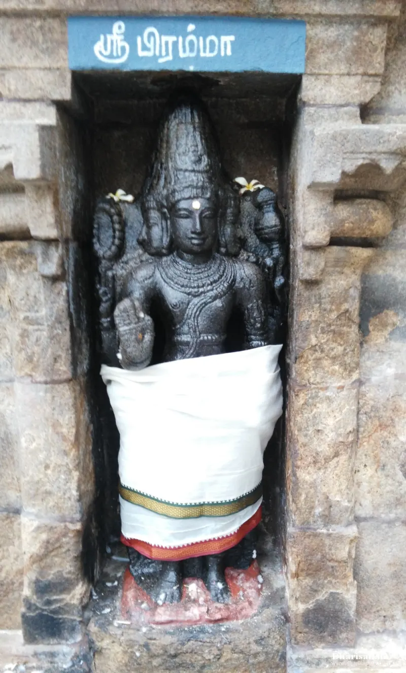 A black stone Brahma with several faces in a niche, in a white dhoti, under a Tamil name board
