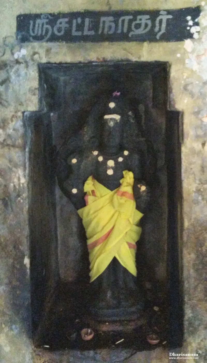 A dark stone idol in a niche wearing a yellow cloth, with a name board above it