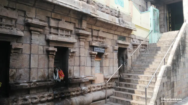 A carved stone wall with small dark openings beside a stone staircase with railings
