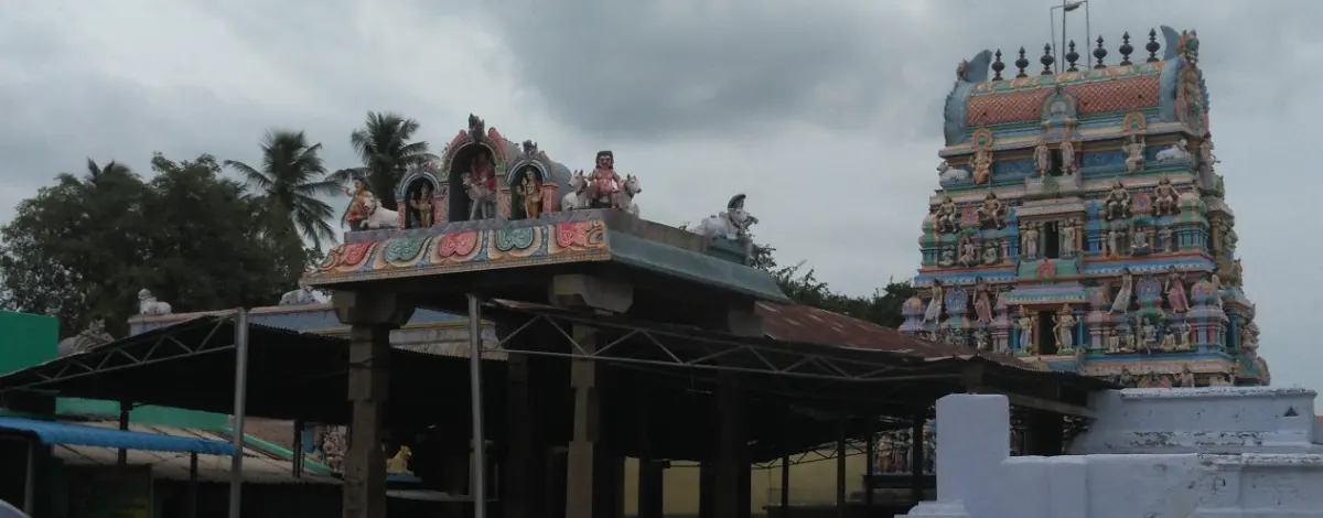 Two painted towers rise behind a pillared hall with a metal roof under a cloudy sky