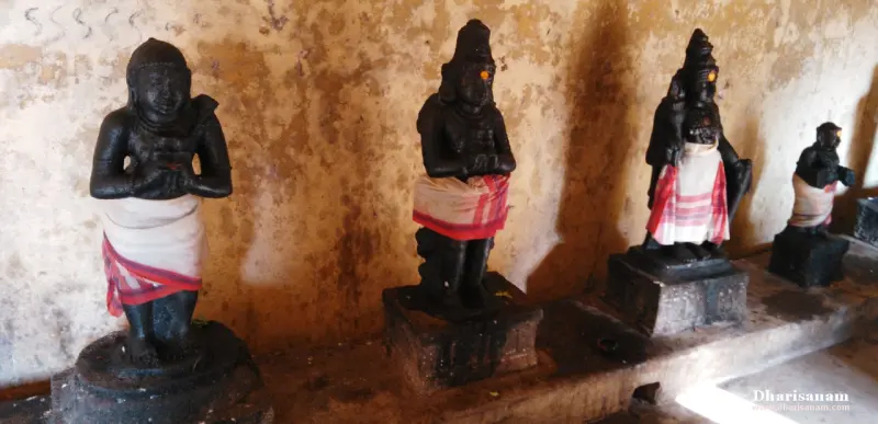 Four dark stone figures in a row, hands joined, each wearing a red and white striped cloth