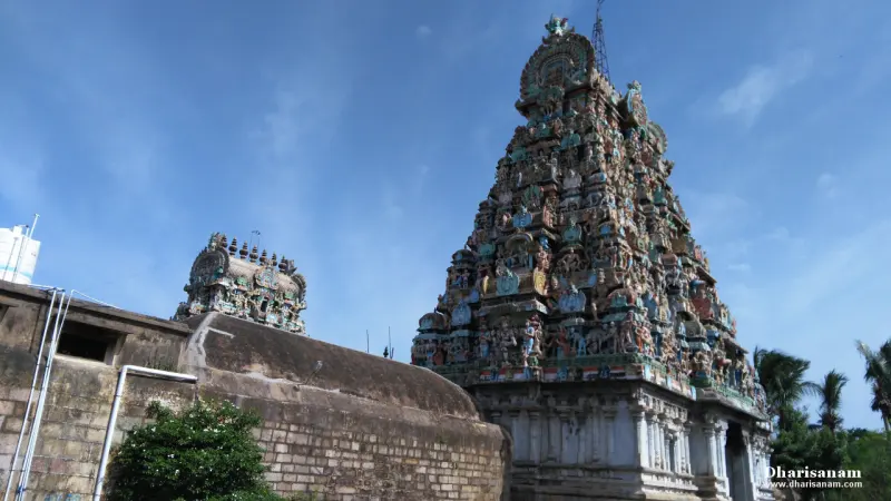 A tall tiered gopuram with painted figures, and a smaller tower beside a stone wall