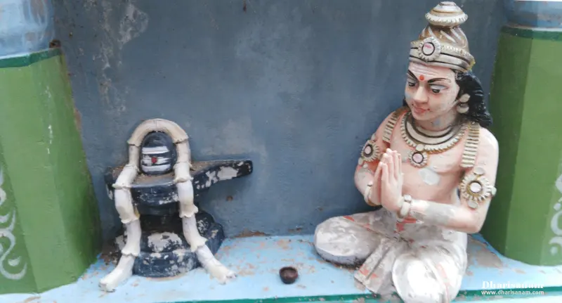 A seated painted figure in prayer next to a small lingam wrapped by a crab's legs