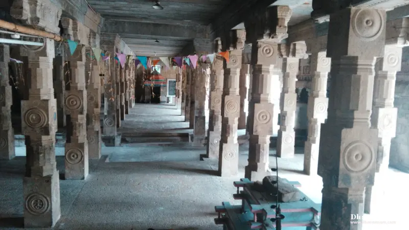 A long stone hall with rows of carved pillars, festive paper flags overhead and a lit shrine at the far end
