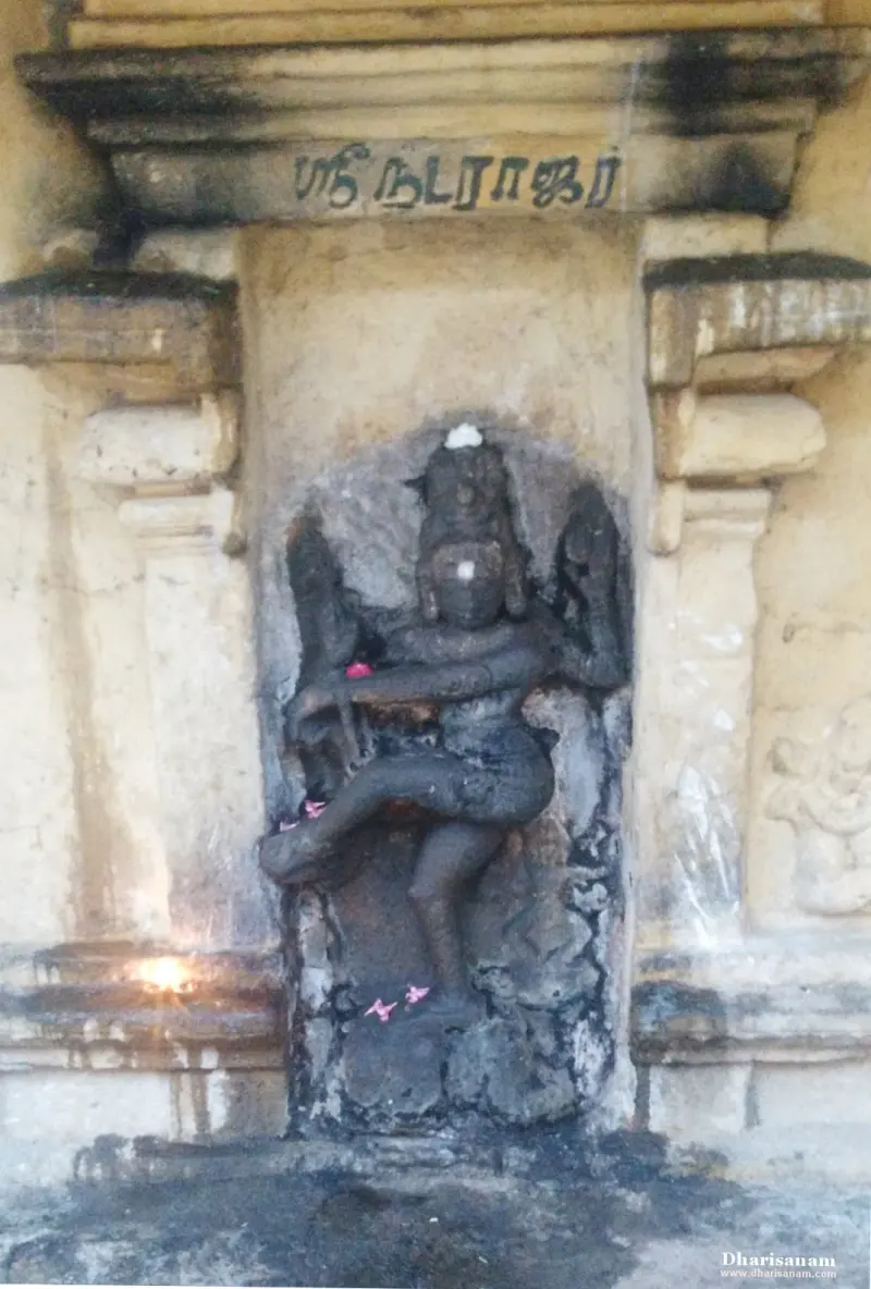 A dark stone Natarajar in a dancing pose in a wall niche, with a Tamil name above it.