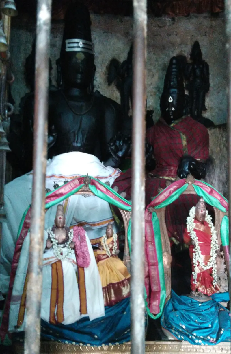 Dark stone deities behind iron bars, with small decorated idols in front