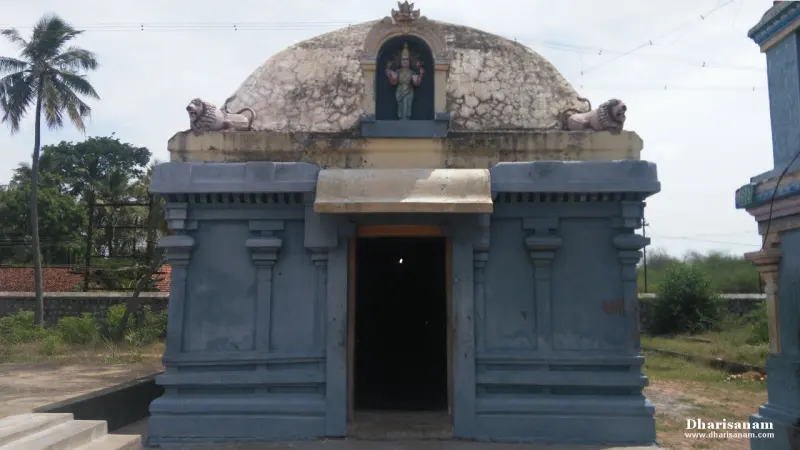 Blue stone shrine with a domed roof and a small figure in a niche above the doorway, with palm trees behind