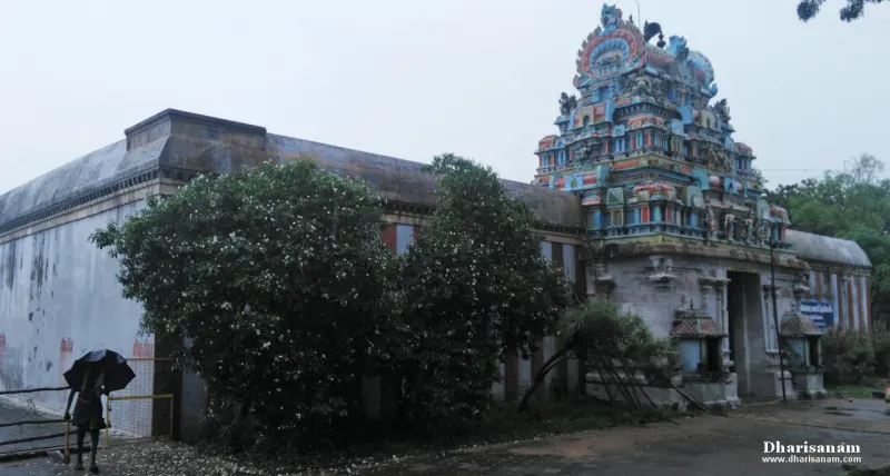 Colourful entrance tower beside a long outer wall, with flowering trees and a person holding an umbrella