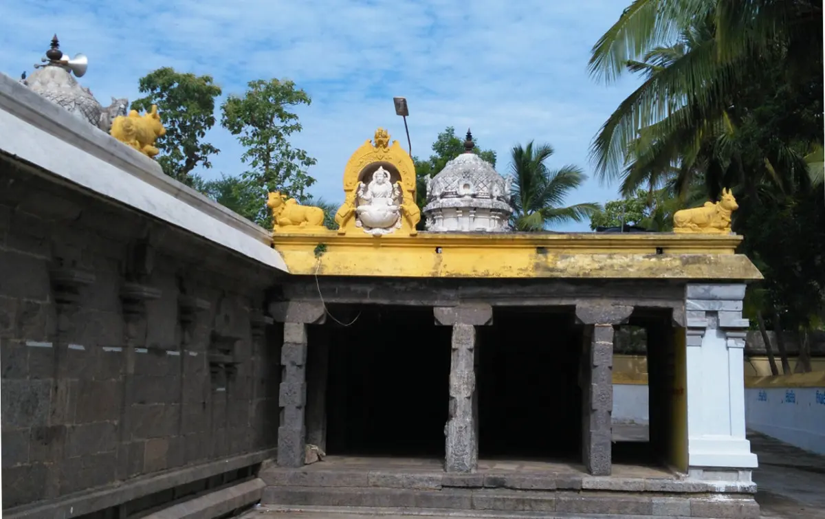 An open pillared stone corridor with a yellow roof edge, a white deity relief above it and small domed towers behind.