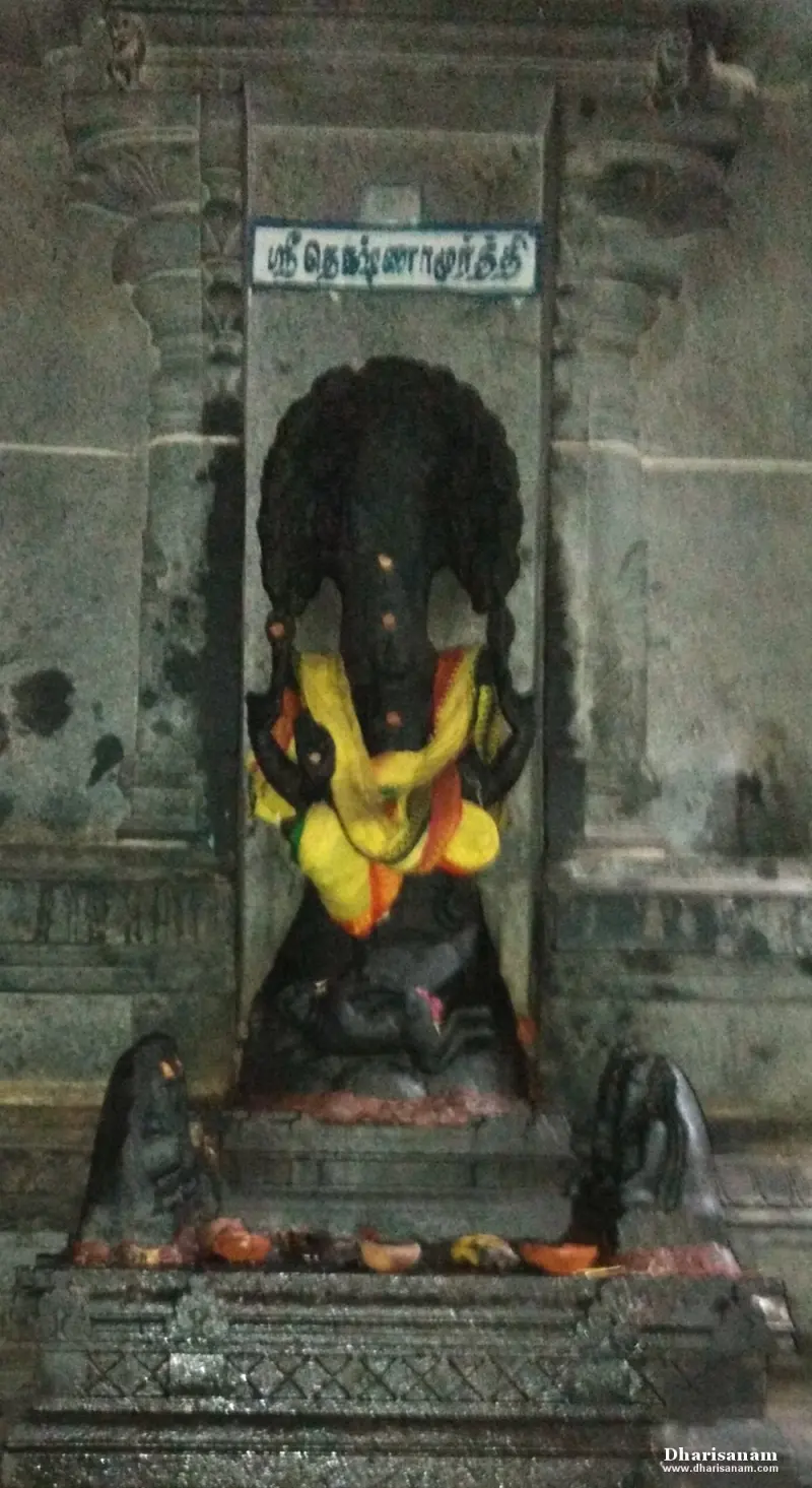 Black stone Dakshinamurthy idol in a niche draped in yellow, with a Tamil name board above