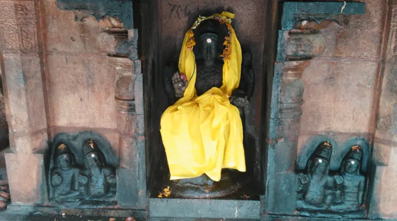 A dark seated idol in yellow cloth with small figures beside it
