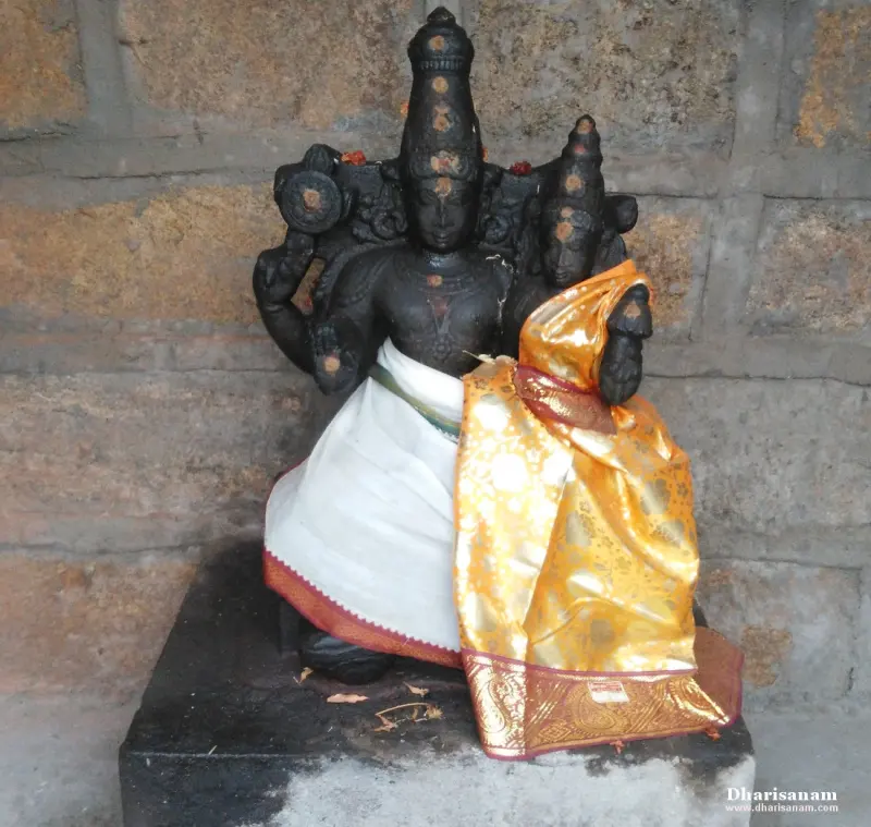 A dark stone idol of a deity holding a discus, seated with a consort, dressed in white and golden silk.