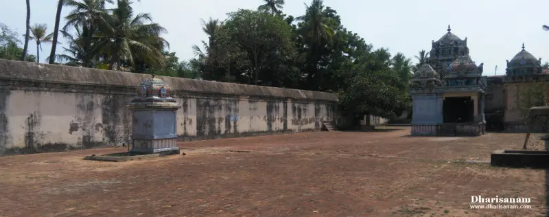Wide paved courtyard with a small shrine, a long wall and trees beyond it