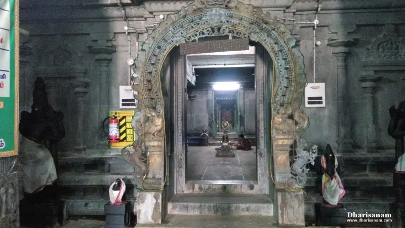 A carved stone arch frames a view down a corridor to a lamp-lit shrine, with idols on either side