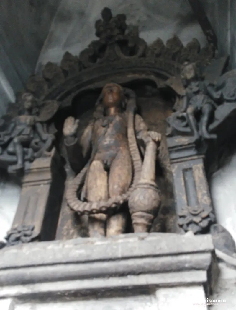 A weathered stone figure standing under an arch, holding a club, with a serpent coiled at its legs