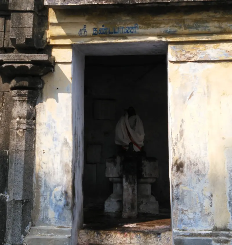 A small shrine with a Tamil name above the doorway and a cloth-draped image inside on a stone base.
