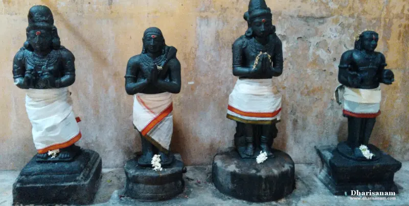 Four black stone figures on stone bases, three with folded hands, wearing white cloth and garlands