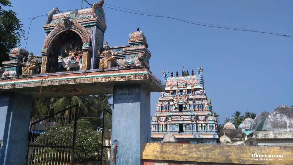 Entrance arch with painted sculptures, a temple tower rising behind it under a blue sky