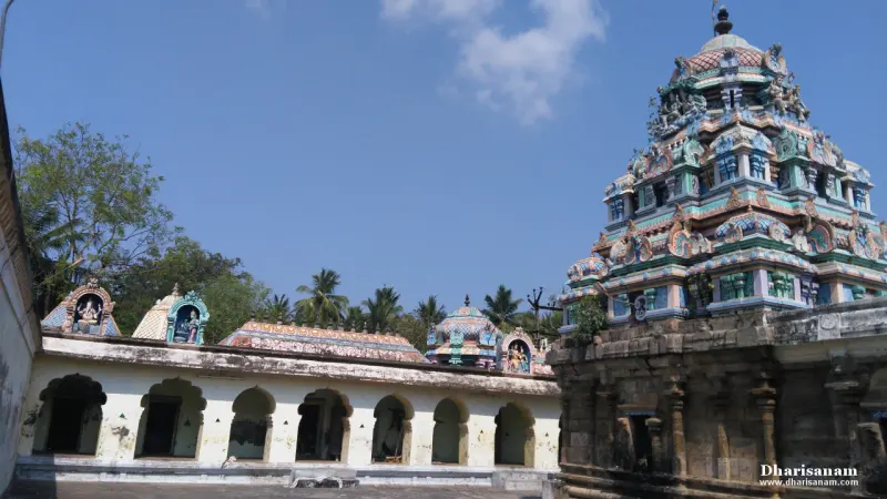 A tiered painted tower beside an arched whitewashed corridor, with small shrines along its roof