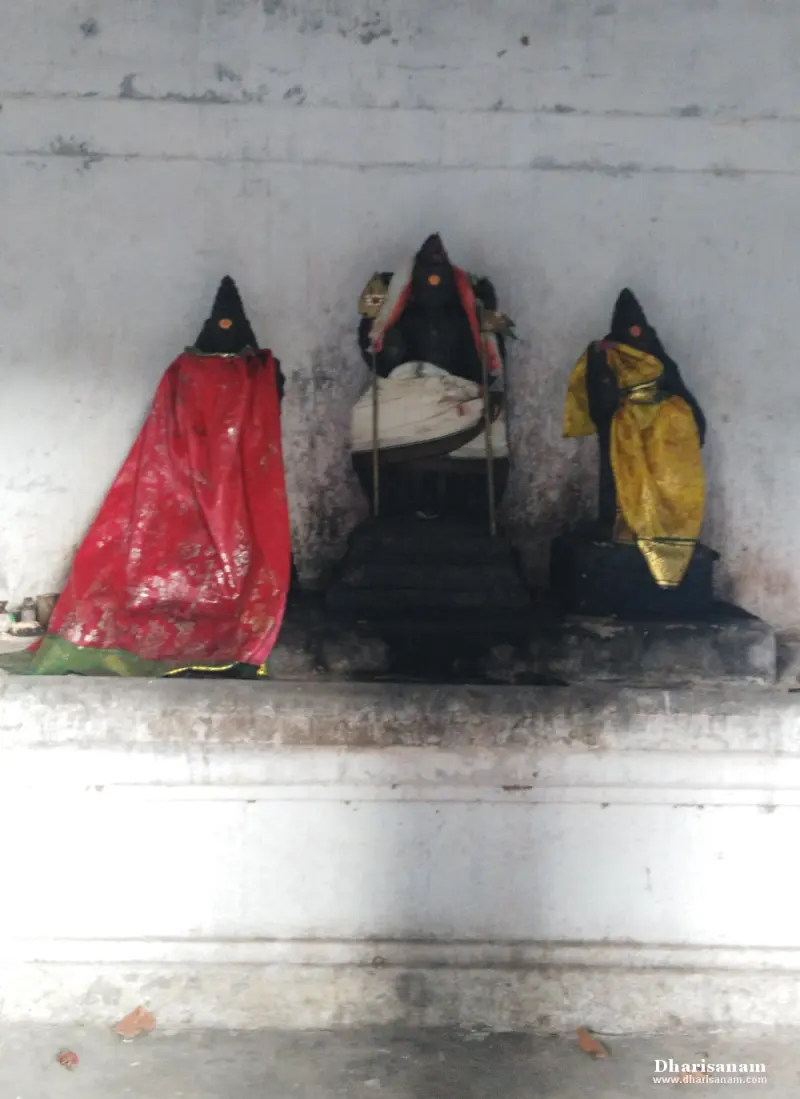 Three black stone idols on a platform, left and right ones in red and yellow cloth, the middle one seated