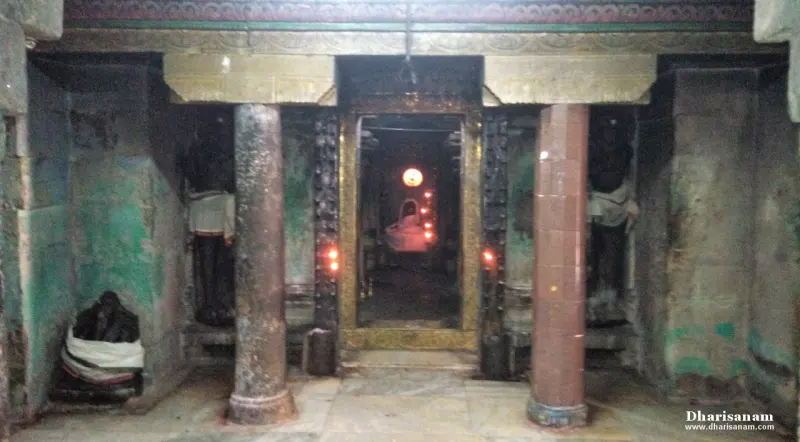 A dim stone passage with two pillars and a lit doorway at the centre