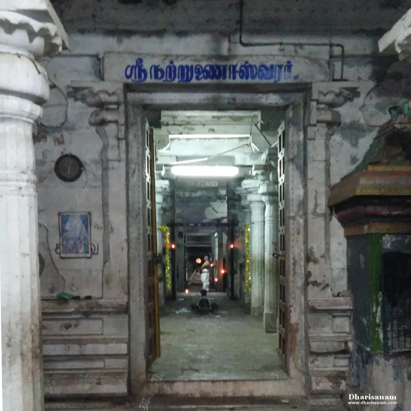 Doorway under a blue Tamil name board, opening onto a lit pillared hall with a priest far inside