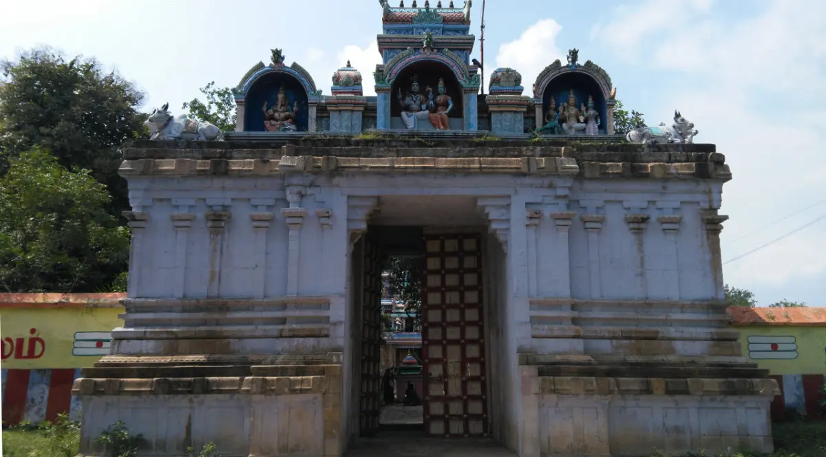 Stone entrance gateway with an open wooden door and painted stucco figures on top