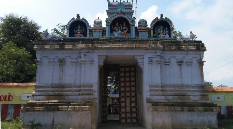 Stone entrance gateway with an open wooden door and painted stucco figures on top