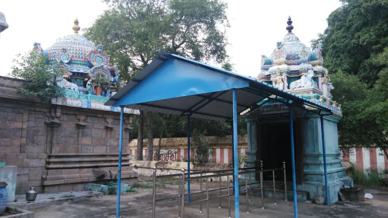 A blue-roofed shelter between two painted shrine towers, one with a stone wall at left.