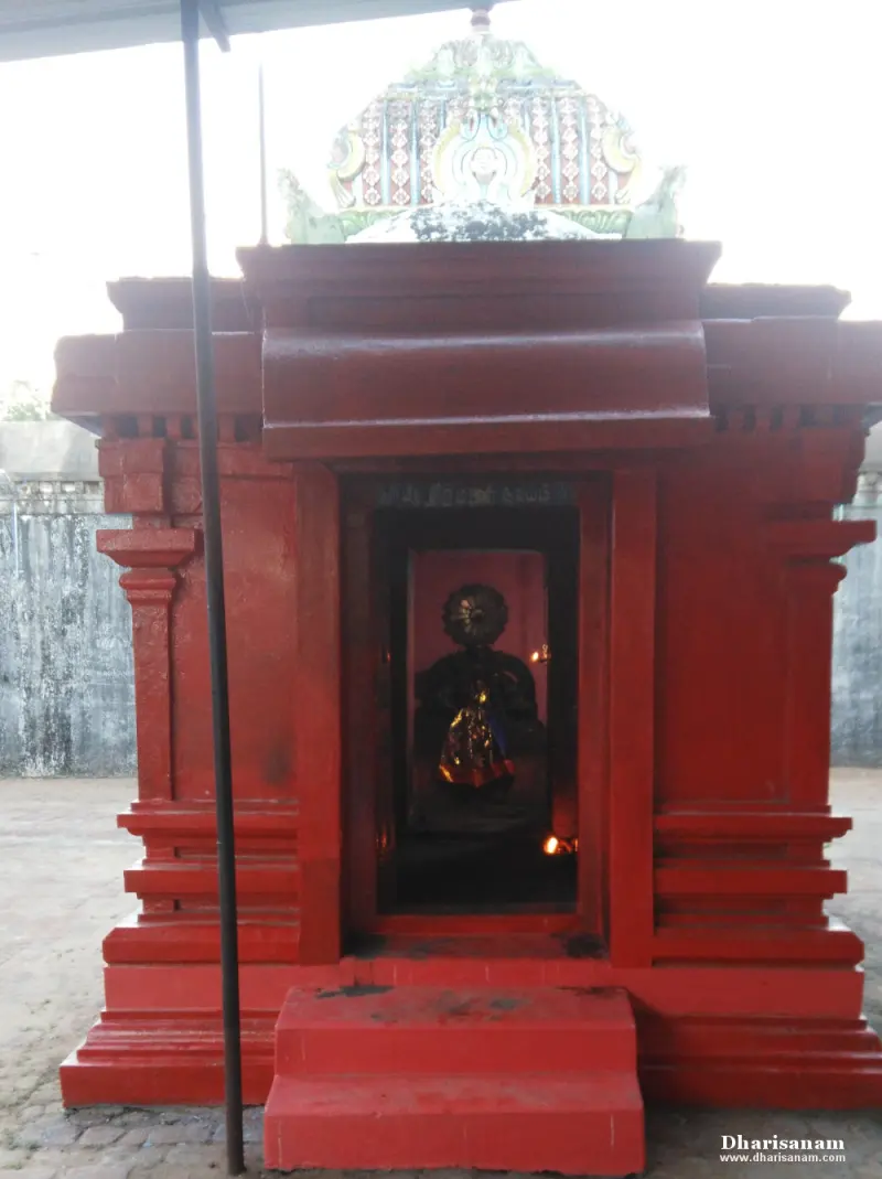 A small shrine painted red stands on a paved floor, with a lit idol inside and a decorated crest above