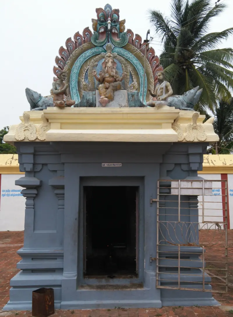 Grey shrine with a dark doorway; a seated Vinayakar and two attendants are on its roof.