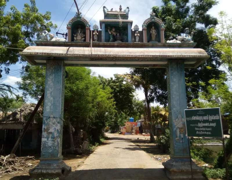 Pillared arch topped with painted figures over a village road, with a green name board at the right
