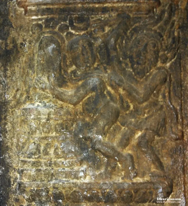 A weathered carved relief showing two figures close together on a raised base.