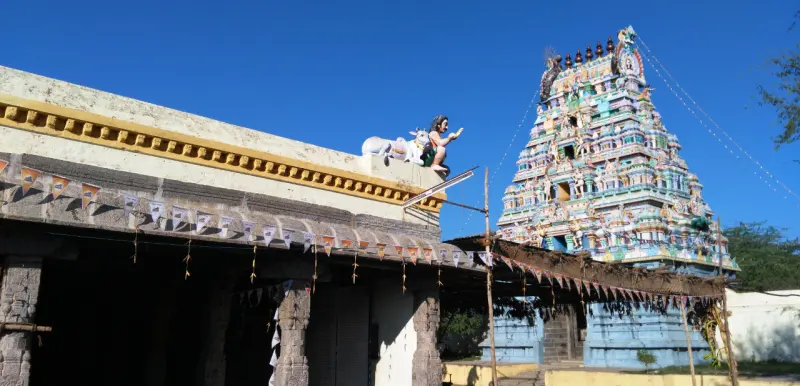 A colourful tiered tower at right and a pillared hall at left with a white bull figure on its roof
