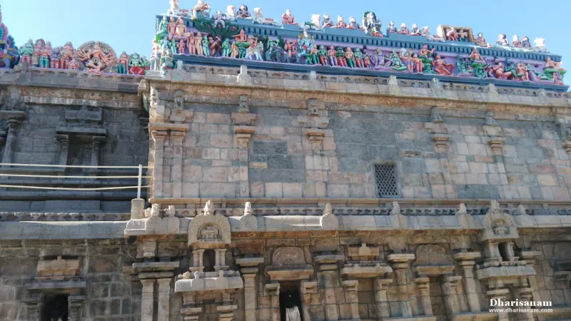 A tall stone wall with carved pilasters and a row of painted figures along the roof edge.