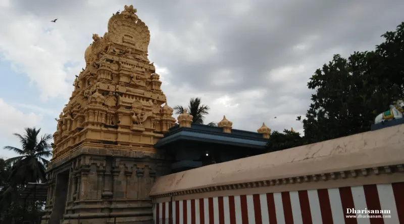 A tiered sandstone tower under a cloudy sky, beside a red-and-white striped wall