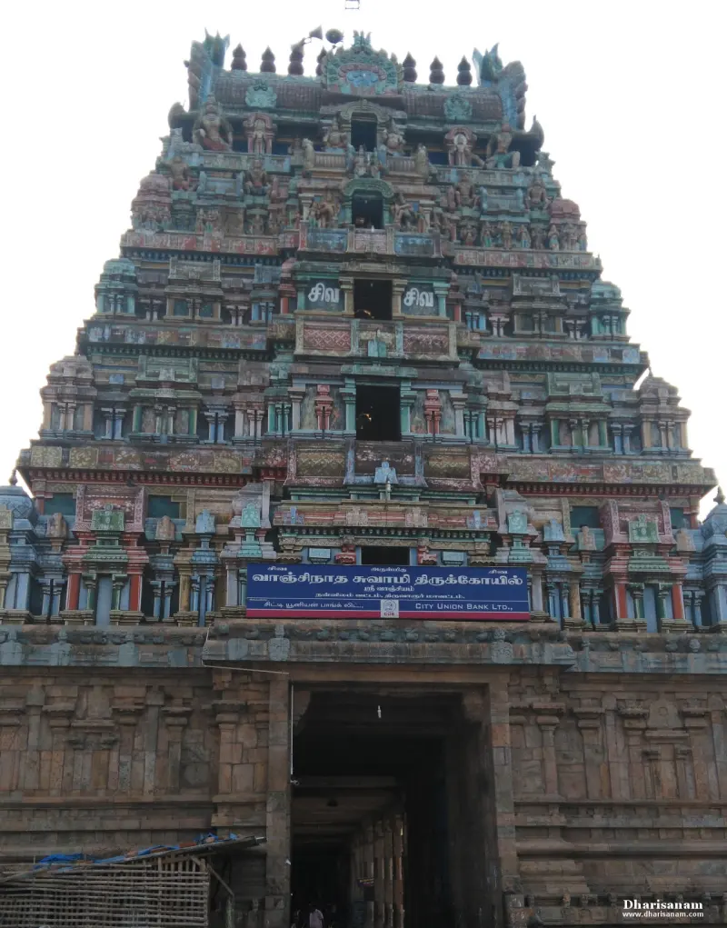 A tall multi-tiered tower with colourful sculptures above a dark stone gateway and a name board