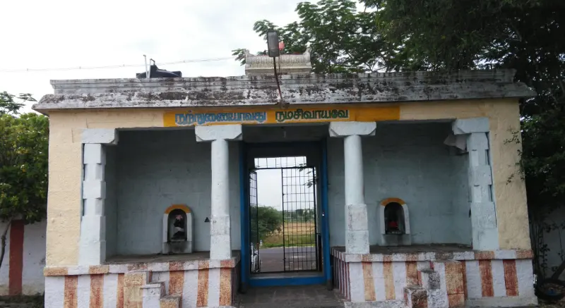 A small pillared porch with a Tamil inscription band above, two small niches with figures, and a gate to a field.