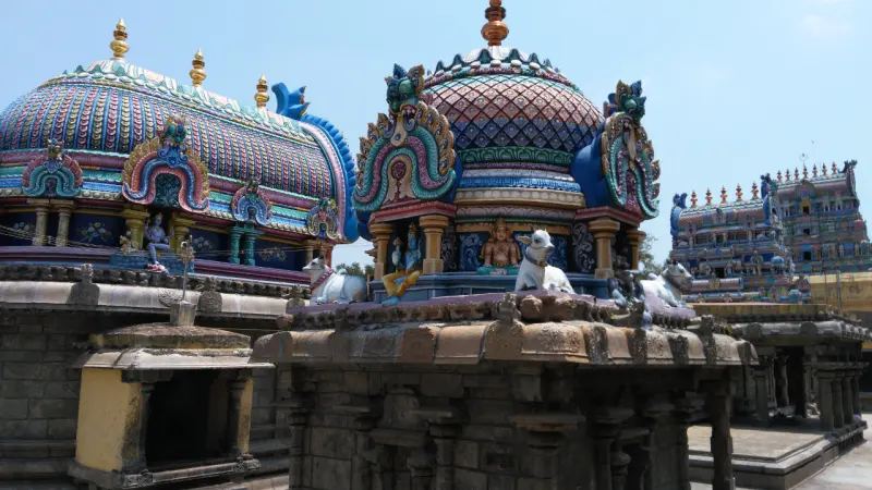 Painted shrine domes with white bull statues; a tall tower stands in the background under a blue sky