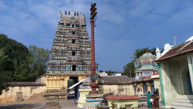 A tiered painted tower, a tall red flagstaff and a domed shrine against a blue sky, with two women at right.