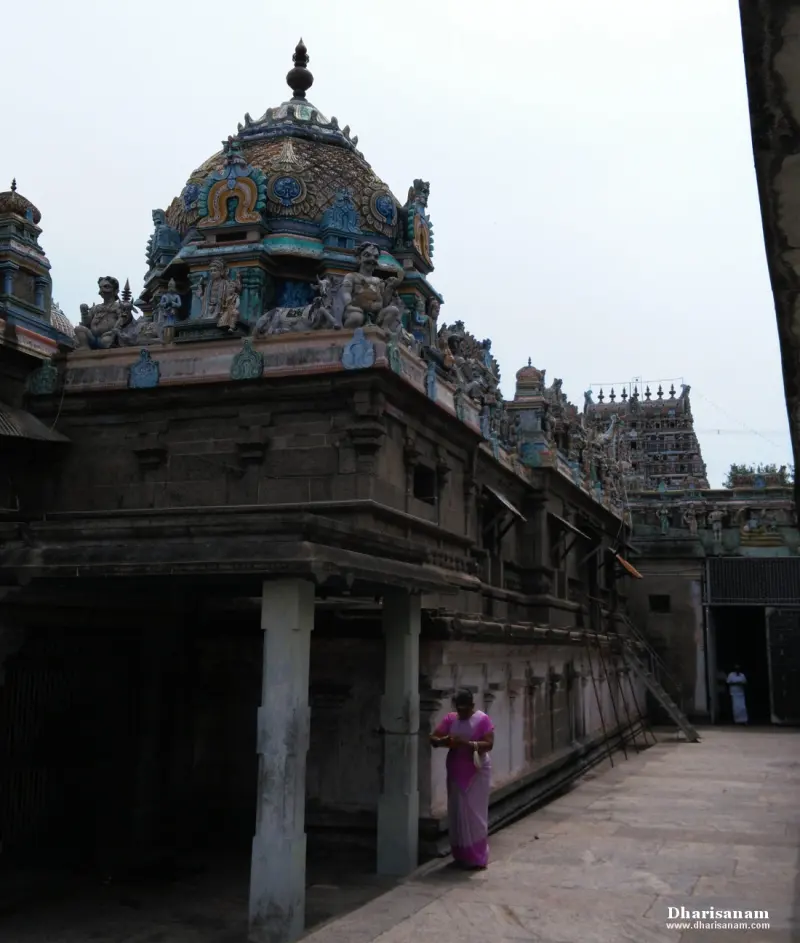A domed shrine roof with painted figures above a stone wall, a woman in a pink saree in the corridor